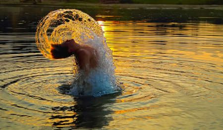 Poseidon Rises  Teenaged male leaping out of the water, with a sunset in the background  の写真素材