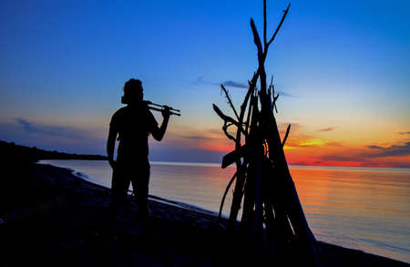 The Photographer  Silhouette of a photographer holding a tripod watching the sunset over the watery horizon  の写真素材