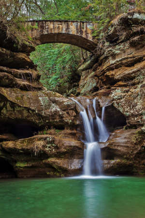 Serene waterfall with stone footbridge crossing. Old Mans Cave . Hocking Hills State Park. Logan, Ohioの写真素材