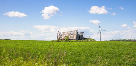 Changes: Old Meets New. Abandoned barn in a field with a new wind turbine in the background. Shot in panoramic orientation with copy space in the foreground.の写真素材