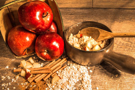 Apple Cinnamon Oatmeal. Fresh hot bowl of cinnamon oatmeal surrounded by cinnamon sticks, apples, and raw oatmeal on a rustic wood background.の写真素材