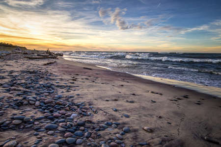Scenic Windy Beach Sunset Background. Wide sandy beach with waves crashing on the shore at Whitefish Point on the coast of Lake Superior. Wide angle with rocks in foreground and waves at the horizon.の写真素材
