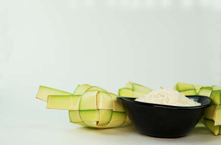 Ketupat rice casing made from young coconut leaves for cooking rice on a white background. Rice in blck bowl.Isolated white bckground.Selective focus.の写真素材