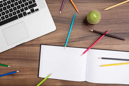 Desk with open laptop, cactus, notebook and pencils in many colors