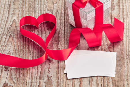 Brown wooden background with silver box, letter and ribbon curled into heartの写真素材