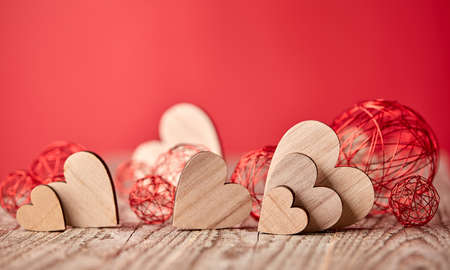Different size heart figures on wooden table and red background with bauble