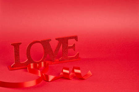 Red background with big glitter love sign with ribbon curled into heart and messageの写真素材