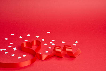 Red background with ribbon curled into heart and white confettiの写真素材