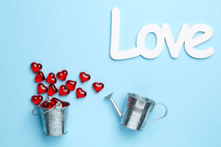 Plain blue background with love and composition of watering can and bucket full of hearts