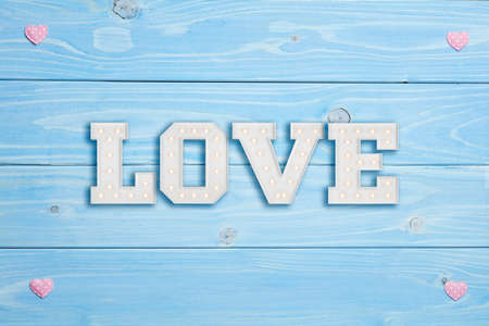 Texture of pink heart shaped figures into frame with love phrase inside, on blue wooden backgroundの写真素材
