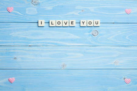 Texture of pink heart shaped figures into frame with I love you phrase inside, on blue wooden backgroundの写真素材