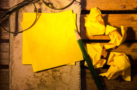 yellow blank paper with crumpled paper with glasses with pencil on an old book on wood pettern background の写真素材