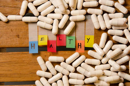 Healthy alphabet and capsule drug with little red heart on wood pattern backgroundの写真素材