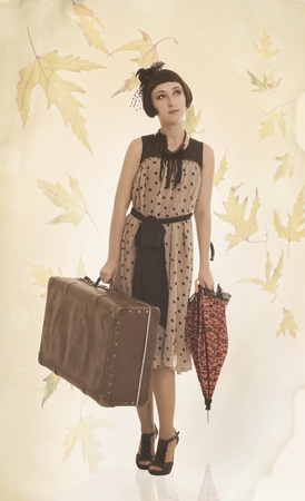 Beautiful brunette girl with umbrella and old suitcase isolated on autumn background