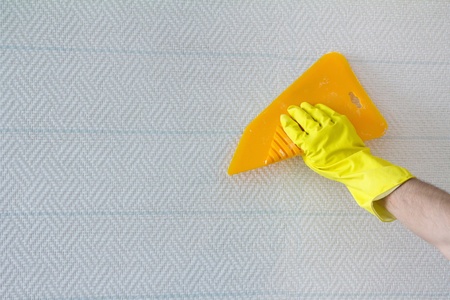 hand in protective gloves with spatula smoothing wallpaper