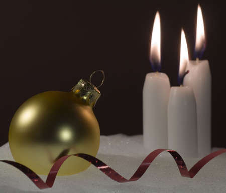 White candles gold ornament and red ribbon sitting in a base of snowの写真素材