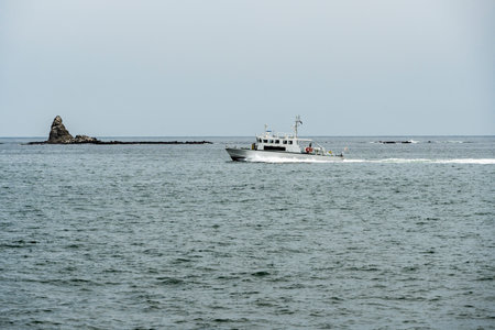 Fishing boat in the sea with rocks in the background and cloudy sky