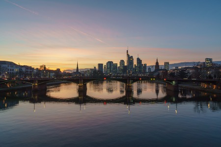 Stunning sunset view of the financial skyline in Frankfurt. Pictures were taken from the Floesserbruecke during blue hour in february. Thus the office rooms already have their lights on and having lots of light effects on the main river.のeditorial素材