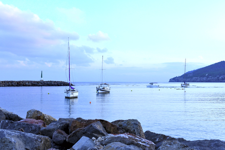 Tranquil sea scene with lighthouse and anchored boats after the sunset.の写真素材