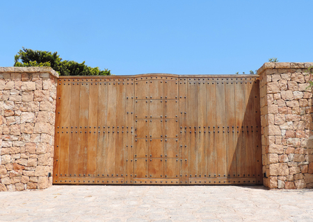 Wooden gate of a mansion with drystone wall and security system.