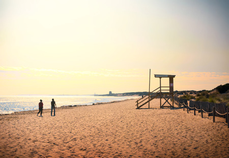 Sunset beach scene with couple walking along along the beach.の写真素材