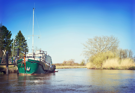 Sunny riverside with marshland and reeds. View from a boat to a river with little pier or jetty in springtime.の写真素材