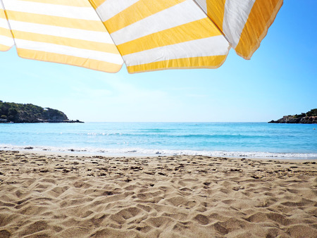 Beach background with yellow and white striped sunshade, beach with no people and turquoise sea with copy space.の写真素材