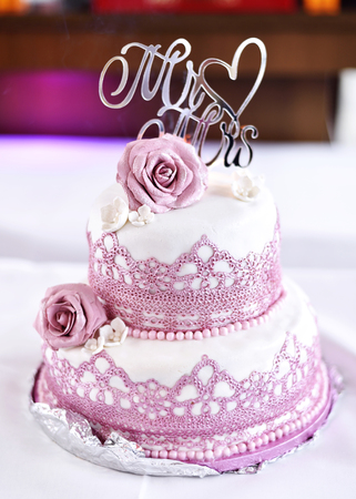 Pink and white wedding cake with roses on a white table.の写真素材