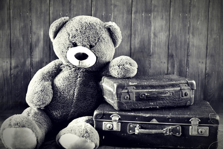 Teddy bear with old suitcases, sitting on a wooden floor with wooden background and copyspace. Travel scene.の写真素材