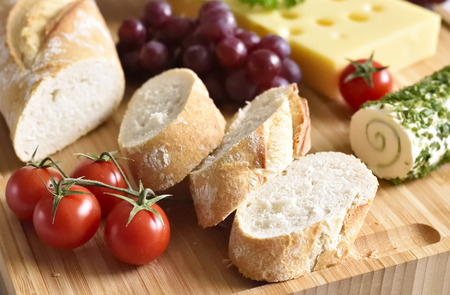 Healthy eating scene of a cheese plate with fresh baguette, fresh tomatoes and fruits. Wooden table, rustic scene.の写真素材