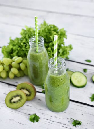 green smoothie, healthy, organic drinks with fresh vegetables and fruits. Two smoothie glasses with drinking straw on a white table. Close-up shot.の写真素材
