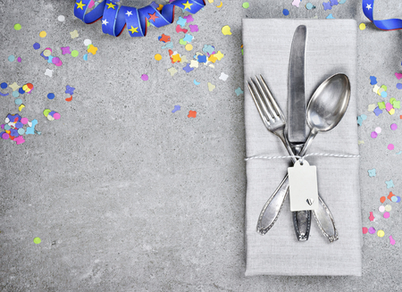 Birthday table setting background with copy space. Concrete background with napkins, silverware and name tag. Cutlery with fork, knife and spoon. Top view, party or event decoration with confetti.の写真素材