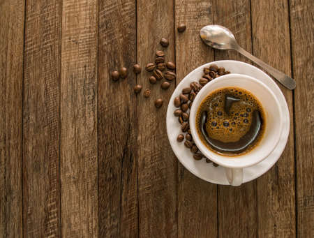 A cup of coffee and coffee beans placed on a wooden background.
