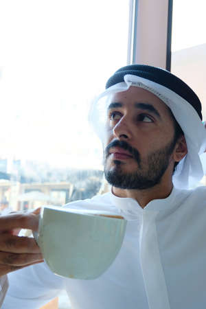 Arab man with coffee cup looking up  wearing Ghutra