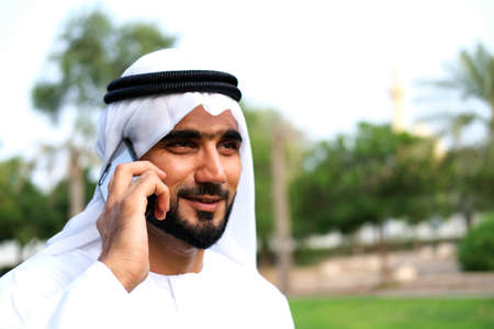Happy Arabic Man talking on his smart mobile phone device with positive face mock up and copy spaceの写真素材