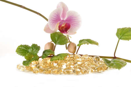 Glossy vitamin pills and flowers against white backgroundの写真素材