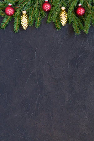 Christmas or New Year border background with Christmas tree branches on a dark textured background and red glass balls decoration. Fir branches, spruce pine cones. Top view with copy spaceの写真素材