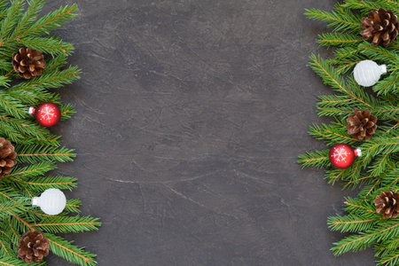 Christmas or New Year festive background with Christmas tree branches on a dark textured background and red white balls decor. Frame of fir branches, spruce pine cones. Top view with copy spaceの写真素材
