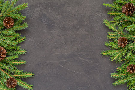 Christmas background with Christmas tree branches on a dark textured background. Frame of fir branches, spruce pine cones. New Year border on black background. Top view with copy spaceの写真素材
