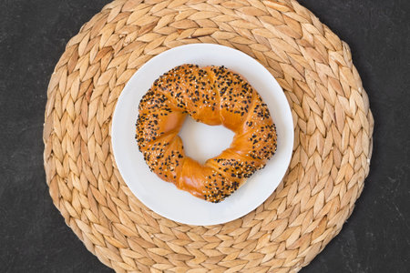 Turkish bagel simit with sesames on white plate and wicker napkin on black background. Top viewの写真素材