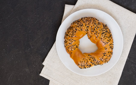 Delicious Turkish bagel simit sprinkled with white and black sesame seeds on a white plate and linen napkin, dark background. Top view, copy spaceの写真素材