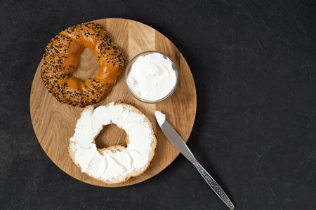 Bagel and cream cheese as a concept for breakfast. Wooden tray, black background, top view, copy space.の写真素材