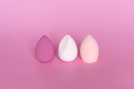 Three colorful beauty blenders or makeup sponges on pink background. Cosmetic tool concept.の写真素材