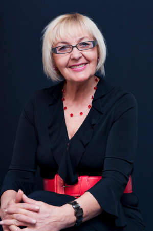 Studio portrait of sitting smiling attractive blonde mature woman with eyeglasses and red belt