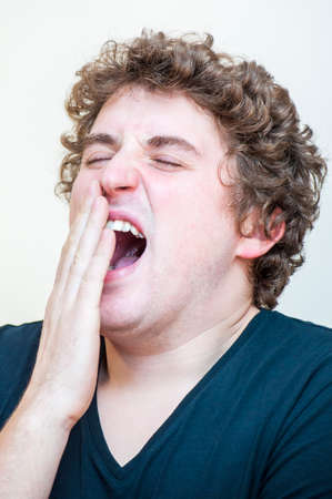Portrait of young Caucasian Ethnicity tired yawning curly man covers his open mouth on white background.の写真素材