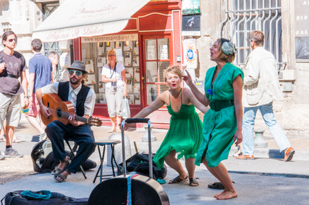 Avignon, France - July 24, 2011: Artists performing outdoors during Avignon Festival. Music band, two girls in green dresses are singing and dancing and one boy is playing guitar on the street.のeditorial素材
