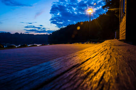 Lake beach bench by sidewalk at night illuminated with street lantern. Lantern had use in human life for a very long time.の写真素材