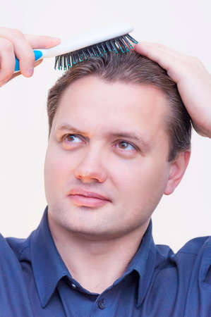Portrait of young Caucasian Ethnicity man with blue shirt brushing combing hair with hairbrush on...