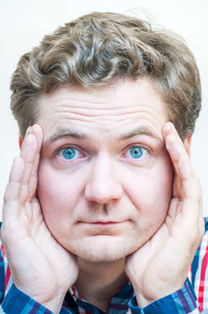 Portrait of young Caucasian Ethnicity blue-eyed man covers his face from sides with two hands on white background.の写真素材