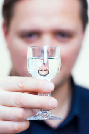 Portrait of young Caucasian Ethnicity man with blue shirt and his upside down reflection in Vodka...